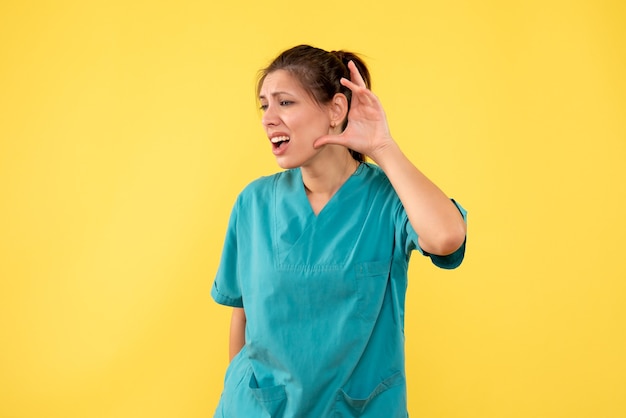 Free photo front view female doctor in medical shirt listening on yellow background