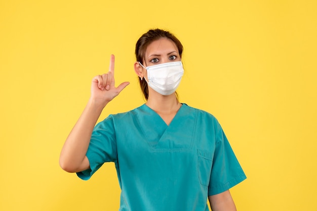 Front view female doctor in medical shirt and mask on yellow background