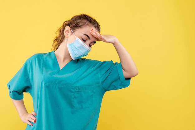 Front view female doctor in medical shirt and sterile mask on yellow desk pandemic color health uniform covid-19 virus