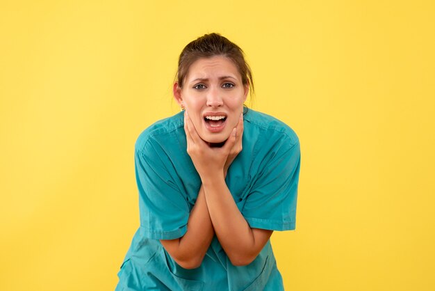 Front view female doctor in medical shirt suffering from toothache on the yellow background