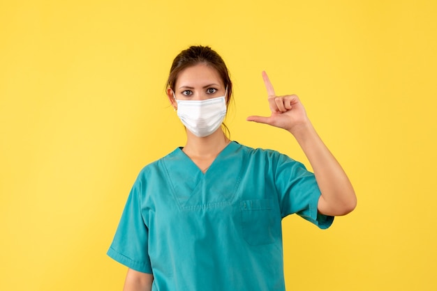 Front view female doctor in medical shirt with sterile mask on yellow background