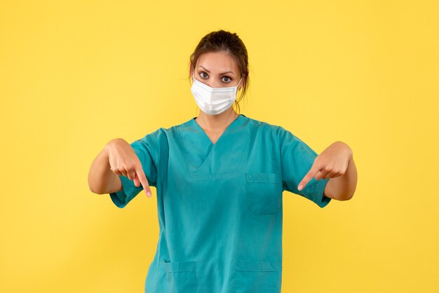 Front view female doctor in medical shirt with sterile mask on yellow background