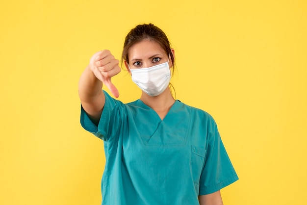 Front view female doctor in medical shirt with sterile mask on yellow background