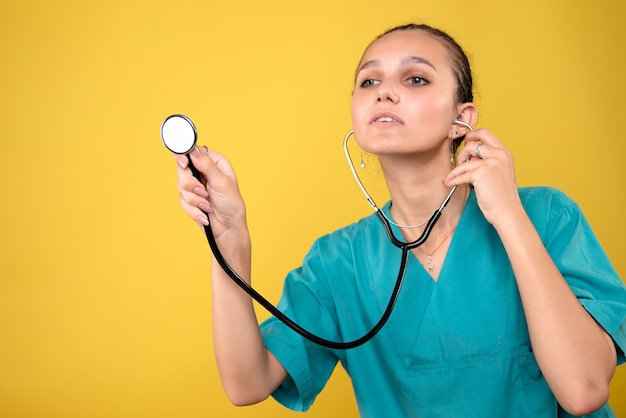 Front view of female doctor in medical shirt with stethoscope on the yellow wall