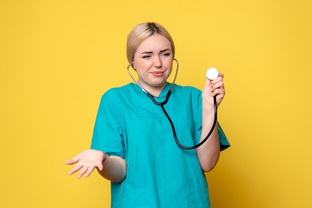 Front view of female doctor in medical shirt with stethoscope on yellow wall