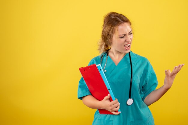 Front view of female doctor in medical suit holding different analysis on yellow wall