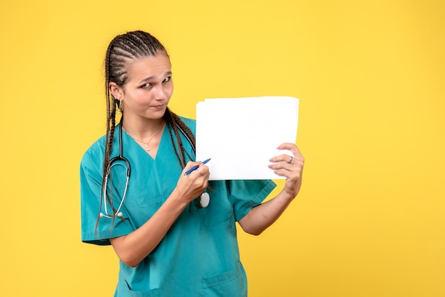 Front view of female doctor in medical suit holding papers on yellow wall