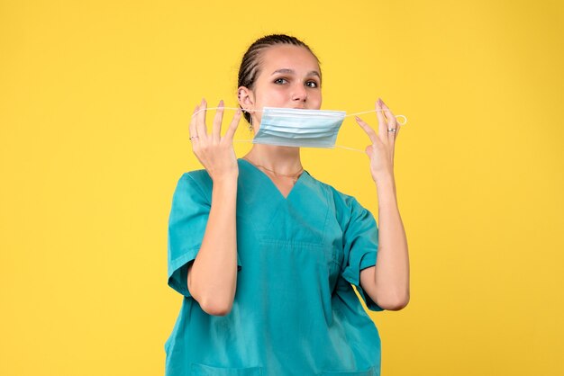 Front view of female doctor in medical suit and sterile mask on yellow wall