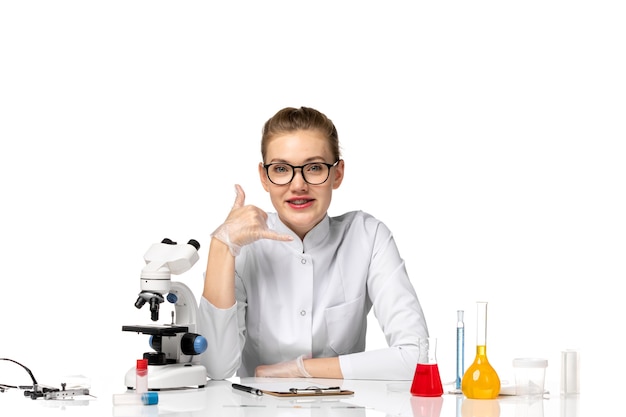 Front view female doctor in medical suit with gloves sitting with solutions on a white space