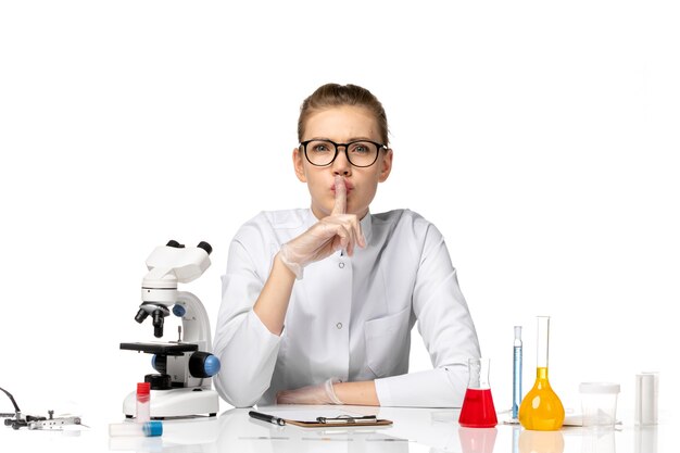 Front view female doctor in medical suit with gloves sitting with solutions on a white space