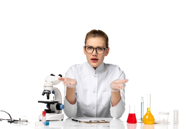 Free Photo front view female doctor in medical suit with gloves sitting with solutions on white space