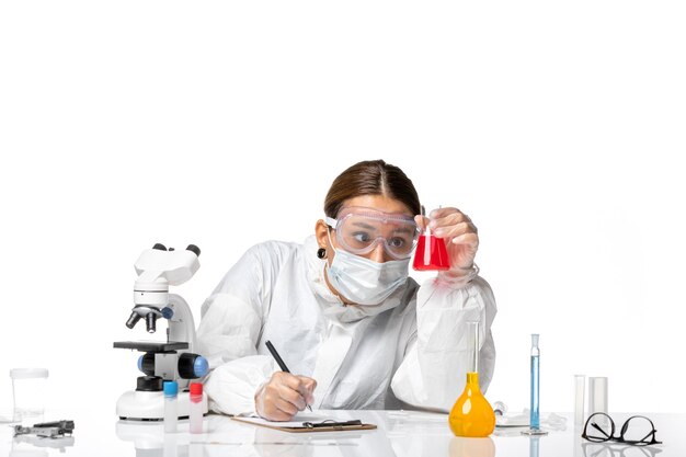 Free photo front view female doctor in protective suit and with mask holding flask with red solution on white background covid virus pandemic coronavirus