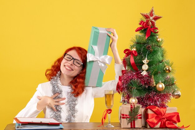 Front view female doctor sitting with christmas presents on yellow background