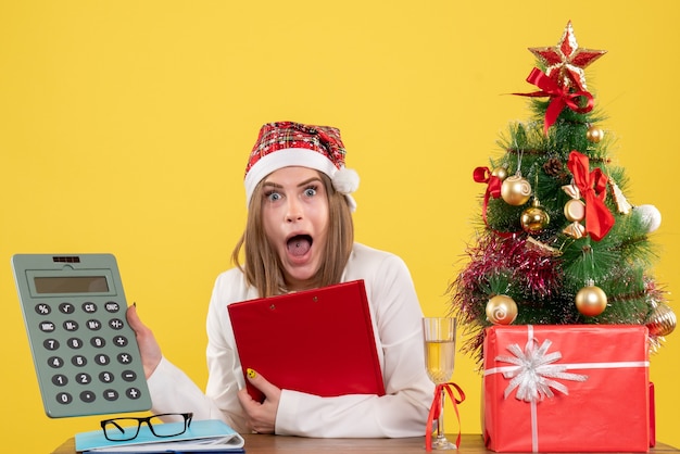 Free photo front view female doctor sitting with xmas presents holding calculator on a yellow background