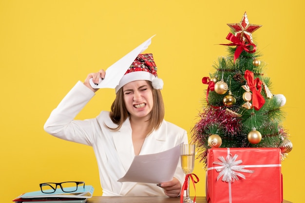 Free photo front view female doctor sitting with xmas presents holding documents on yellow desk