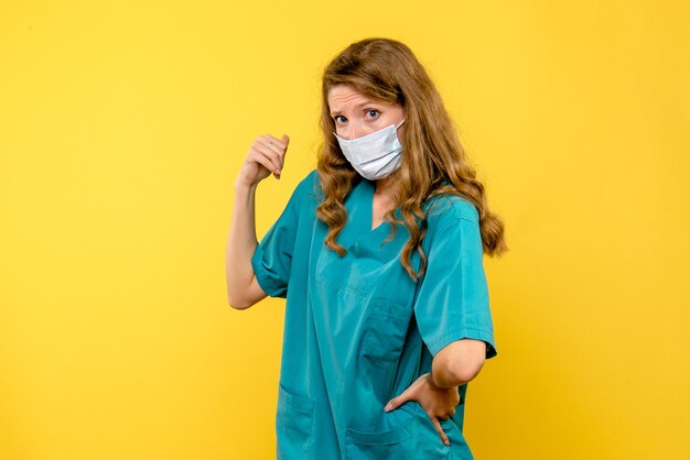 Front view of female doctor in sterile mask on a yellow wall