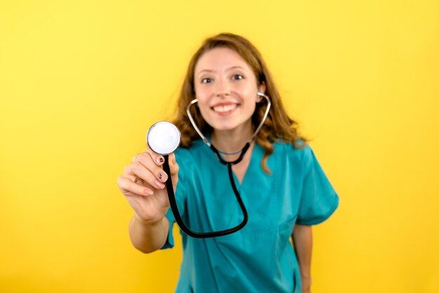 Front view female doctor using stethoscope on a yellow space