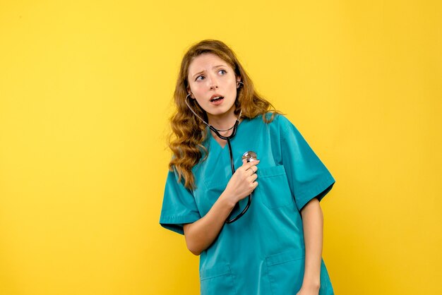 Front view of female doctor using stethoscope on a yellow wall