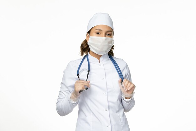 Front view female doctor in white medical suit and mask on light-white wall pandemy virus disease illness medicine