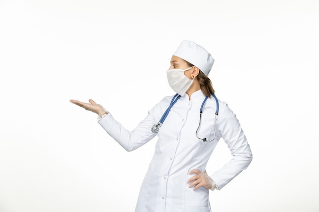 Front view female doctor in white medical suit wearing mask due to coronavirus on light white wall pandemic disease isolation