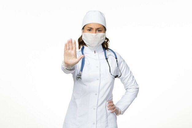 Front view female doctor in white medical suit and wearing mask due to coronavirus on the white wall pandemic disease isolation covid