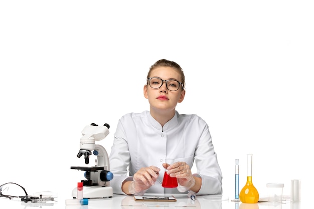 Front view female doctor in white medical suit with gloves holding flask with solution on a white space