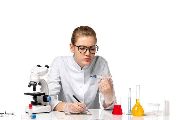 Front view female doctor in white medical suit with gloves holding injection on light-white space