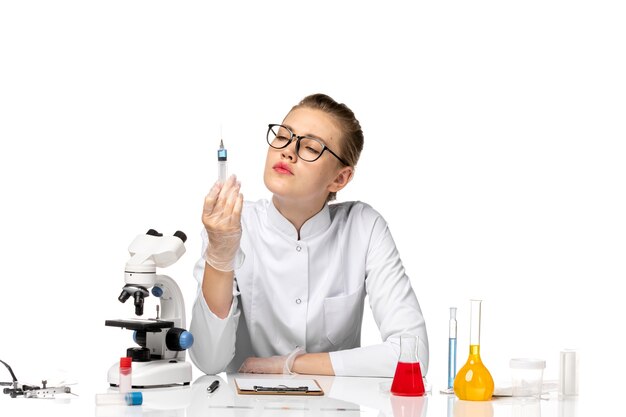 Front view female doctor in white medical suit with gloves holding injection on a white space