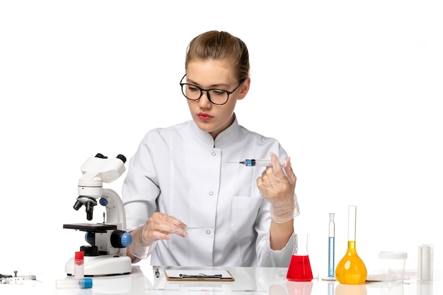 Front view female doctor in white medical suit with gloves using injection on white space