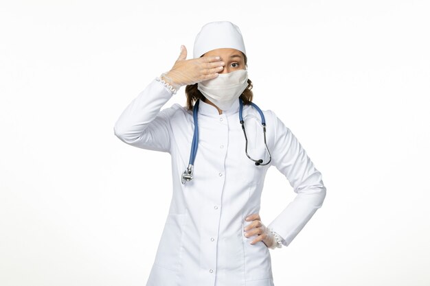 Front view female doctor in white medical suit and with mask due to coronavirus on the white desk pandemic virus disease covid