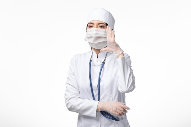 Front view female doctor in white medical suit with a mask due to coronavirus on white wall disease medicine virus pandemic covid-