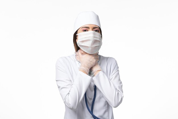 Front view female doctor in white medical suit with a mask due to pandemic having breath troubles on white wall disease medicine virus pandemic covid-