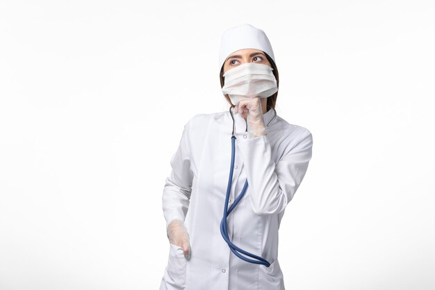 Front view female doctor in white medical suit with a mask due to pandemic thinking on white wall disease health medicine pandemic covid-