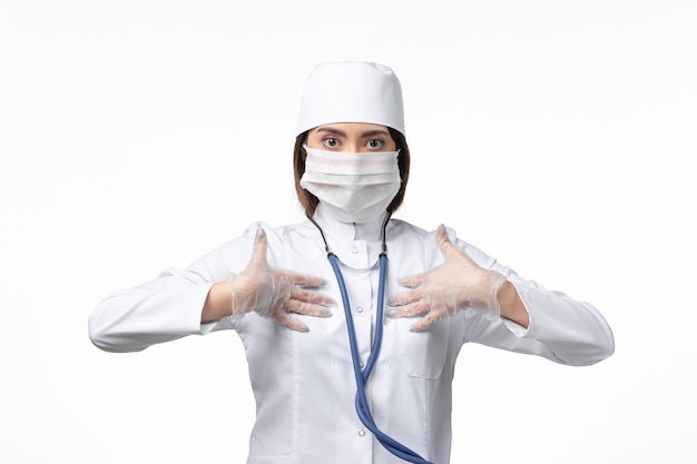 Front view female doctor in white medical suit with a mask due to pandemic on white wall medicine pandemic virus covid-