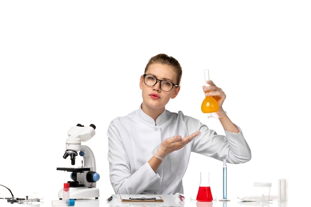 Front view female doctor in white medical suit working with solutions on a white desk