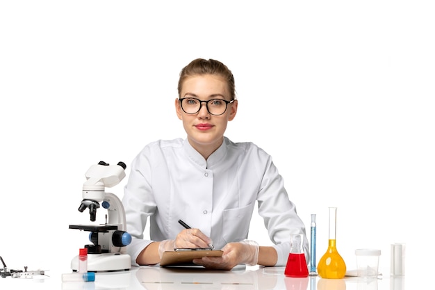 Free Photo front view female doctor in white medical suit working with solutions on a white desk