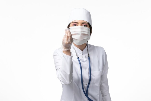 Front view female doctor in white sterile medical suit with mask due to coronavirus on white desk illness covid- disease virus