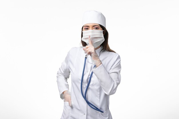 Front view female doctor in white sterile medical suit with mask due to coronavirus on the white desk illness covid- pandemic disease virus