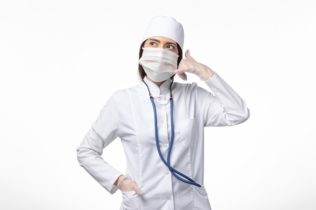 Front view female doctor in white sterile medical suit with mask due to coronavirus on white wall disease illness pandemic covid- virus