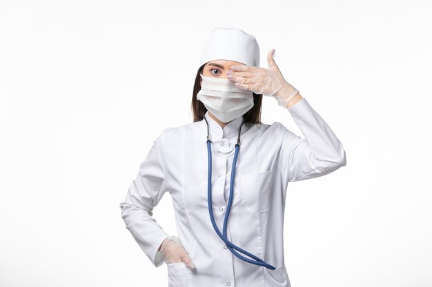 Front view female doctor in white sterile medical suit with mask due to covid- on the light wall illness covid- pandemic virus disease