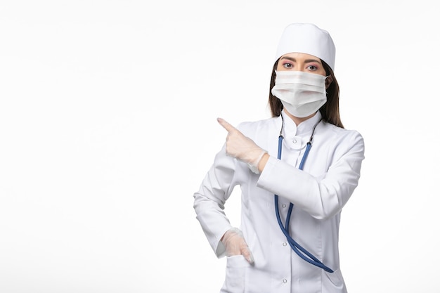 Front view female doctor in white sterile medical suit with mask due to covid- on light white wall illness covid- pandemic disease