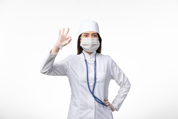 Front view female doctor in white sterile medical suit with mask due to covid- on the white wall illness pandemic virus disease