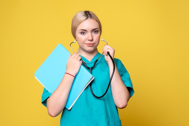 Front view of female doctor with analysis and stethoscope on yellow wall