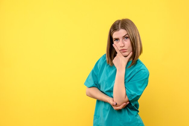 Front view of female doctor with thinking expression on yellow wall