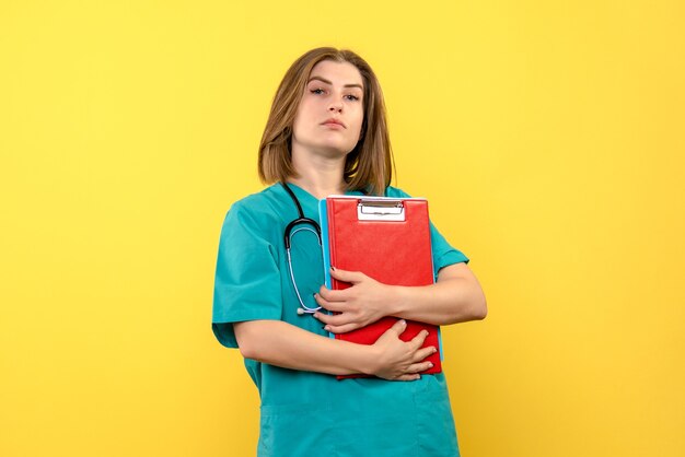 Front view of female doctor with tonometer and files on yellow wall