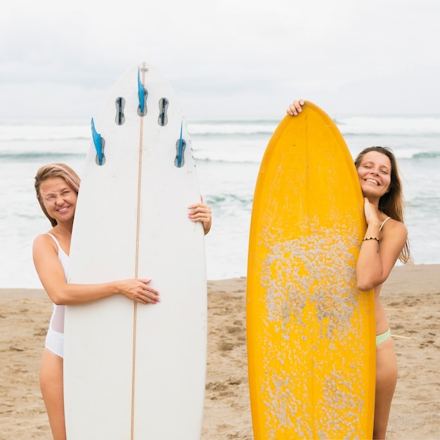 Free photo front view of female friends at the beach posing with surfboards