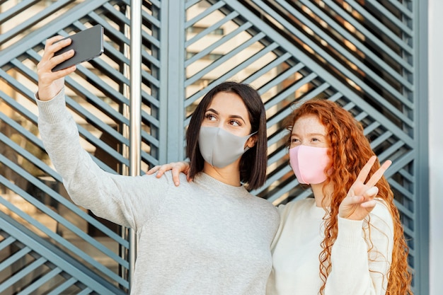 Free photo front view of female friends with face masks outdoors taking a selfie