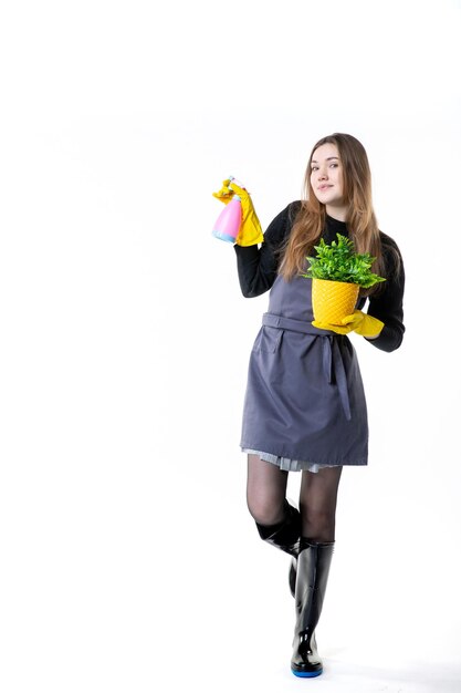 Front view female gardener in yellow gloves watering little plant on white