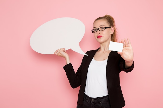 Free photo front view of female office worker in black strict jacket holding white sign and card on the pink wall