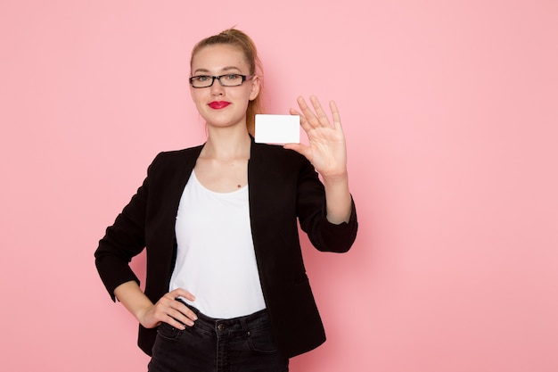 Free Photo front view of female office worker in black strict jacket smiling holding white card on pink wall